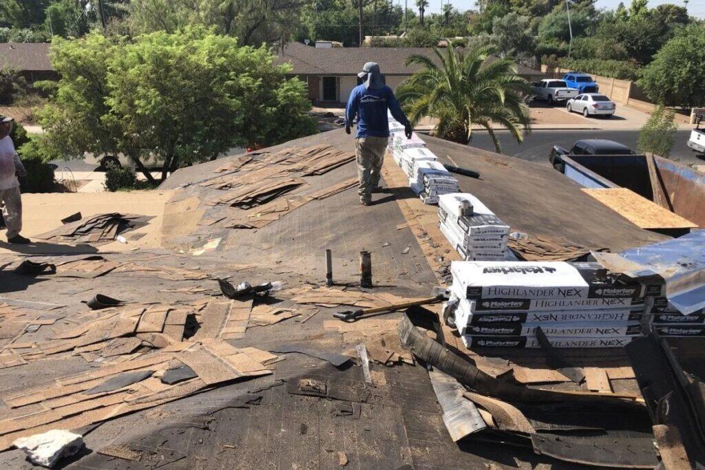 Roofers tearing off old shingles during residential roof replacement, prepping for new asphalt shingle install.